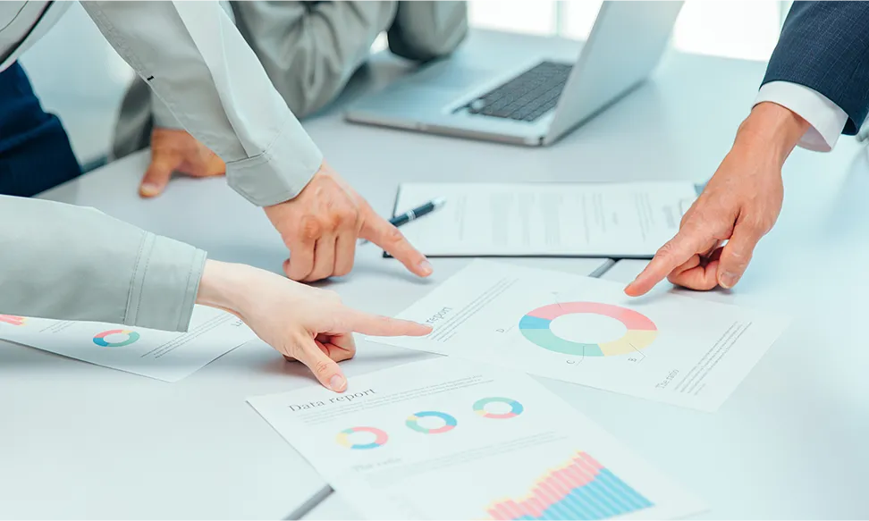 打ち合わせで机の上のデータを指さす写真